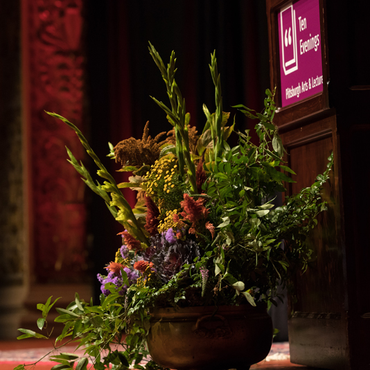 Photo of a beautiful arrangement of flowers in front of the podium at a Ten Evenings lecture in the Carnegie Music Hall